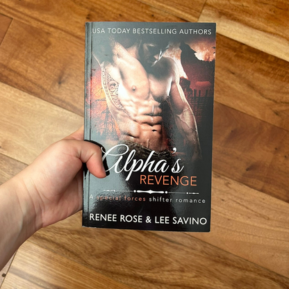 A white person's hand holding a paperback. The book cover features a white, buff, shirtless, tattooed man. In the background is fire and the outline of a wolf. On the top of the cover in white text is "USA Today Bestselling Authors." On the white and orange text is the title "Alpha's Revenge A special forces shifter romance," On the bottom in white text "Renee Rose & Lee Savino"