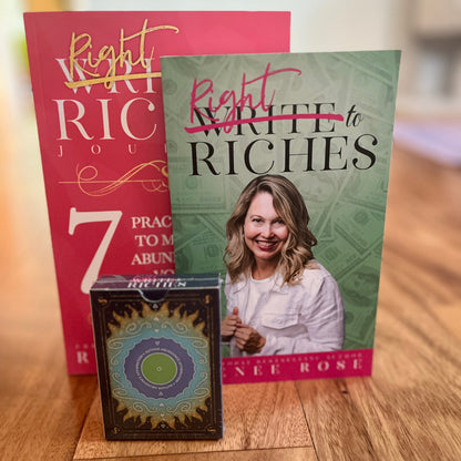A set of self-help and meditation items on a wooden table: a pink book titled 'Write to Riches Journal, a green book titled 'Right to Riches' with a photo of a Renee Rose on the cover, and a decorative deck of Author Abundance Affirmation cards in front.