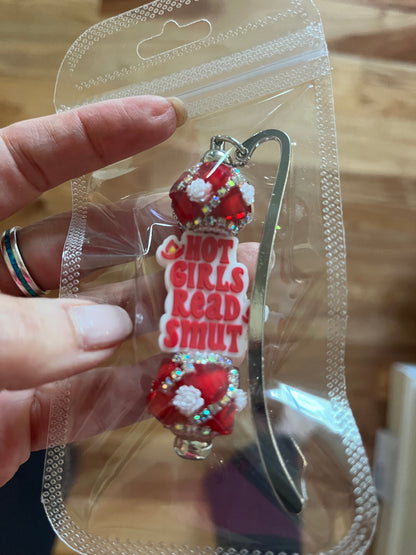 A novelty bookmark with charms and the text 'HOT GIRLS READ SMUT' in red and white, attached to a silver metal post.