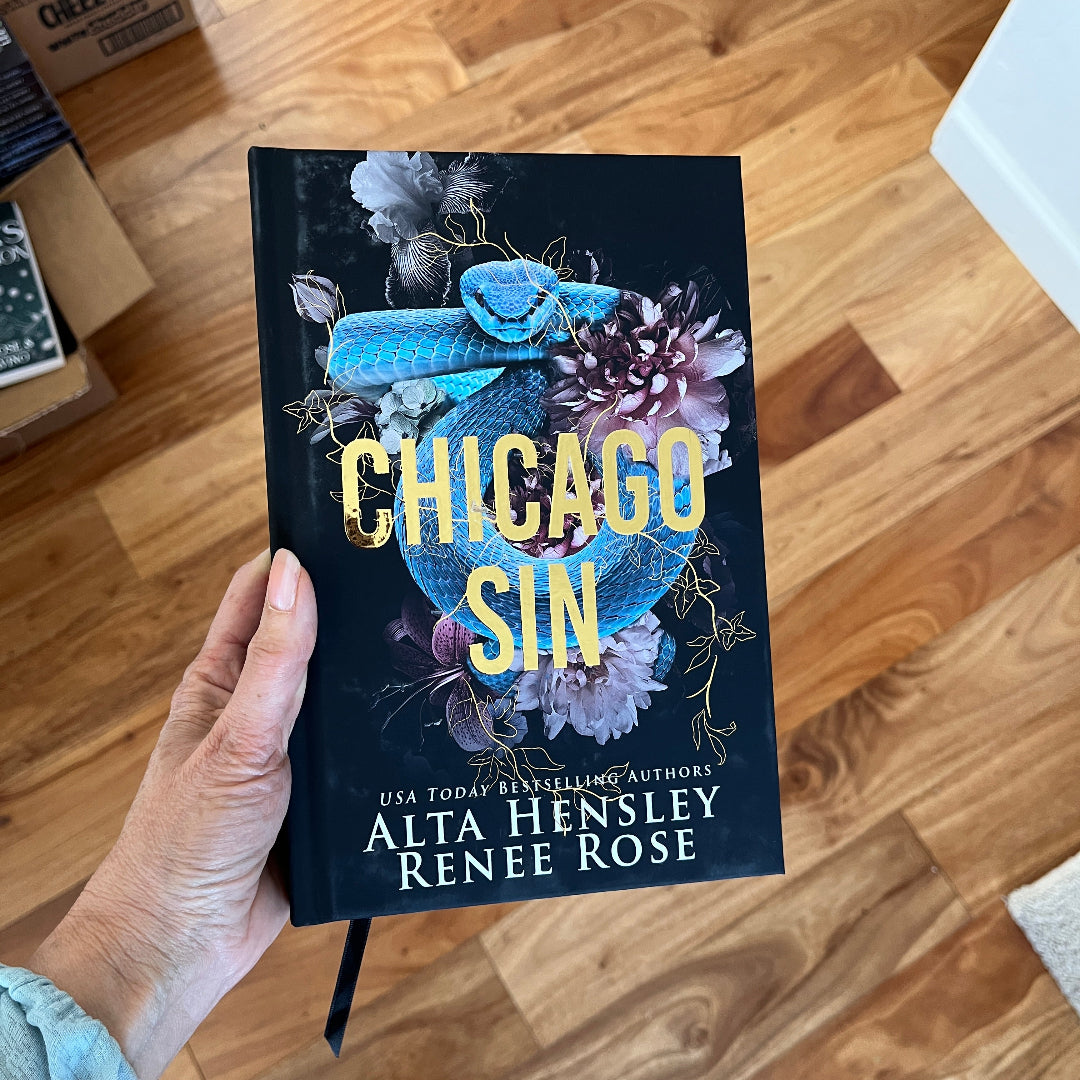 Book titled 'Chicago Sin' held by a person on a wooden floor.