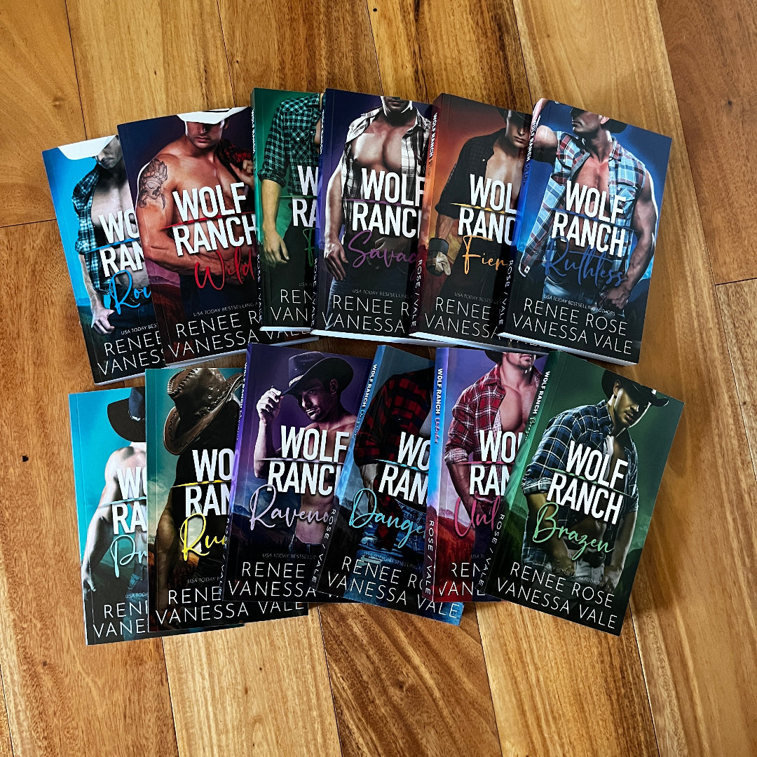 A set of 12 romance novels from the 'Wolf Ranch' series by Renée Rose Vanessa Vale, arranged in two rows on a light brown wooden floor. The books feature various cover designs with wolf imagery and different color themes.