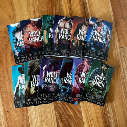 A set of 12 romance novels from the 'Wolf Ranch' series by Renée Rose Vanessa Vale, arranged in two rows on a light brown wooden floor. The books feature various cover designs with wolf imagery and different color themes.