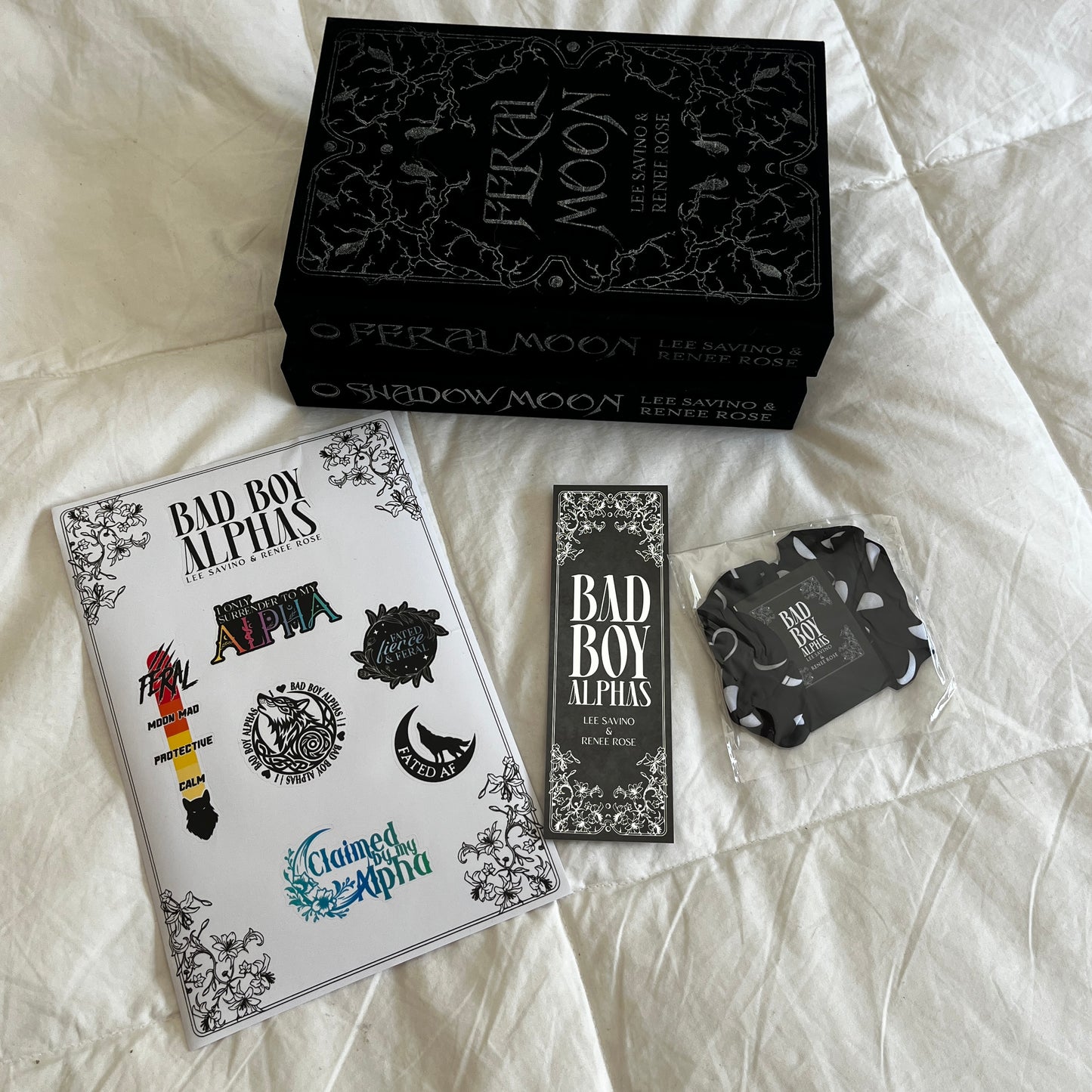 Collection of 'Bad Boy Alphas' merchandise including a box, cards, and stickers on a textured surface.