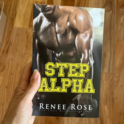 Book titled 'Step Alpha' by Renee Rose held by a hand on a wooden surface