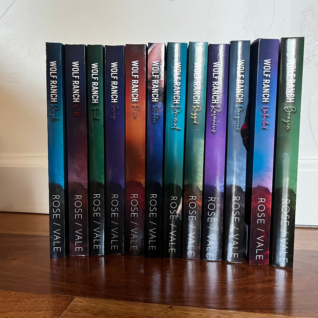 A set of twelve romance novels by Wolf Ranch Books titled 'Rose Vale' arranged in a row on a wooden floor against a white wall.