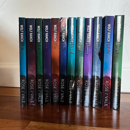 A set of twelve romance novels by Wolf Ranch Books titled 'Rose Vale' arranged in a row on a wooden floor against a white wall.