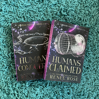 Two books titled 'Human Conquest' and 'Humans Claimed' by Renee Rose on a textured green surface.