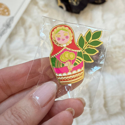 Hand holding a colorful pin with a decorative design on a textured white surface.