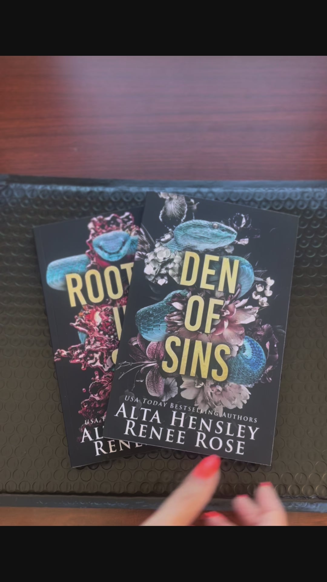 Sped up video. The two books in the Chicago Sin series are fanned out. A white woman -- Renee Rose -- takes the first book "Den of Sins" puts an "Autographed Copy" sticker on it, then draws a big heart, writes "Love and flavors," and signs her name. 