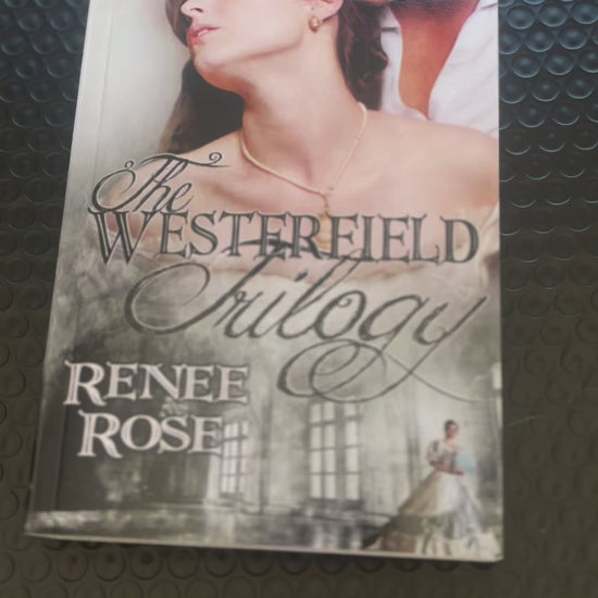 Sped up video. It shows "The Westerfield Trilogy" paperback. A white woman -- Renee Rose -- adds an "Autographed Copy" sticker to the cover, opens the book and signs "Love and scandals, Renee Rose"