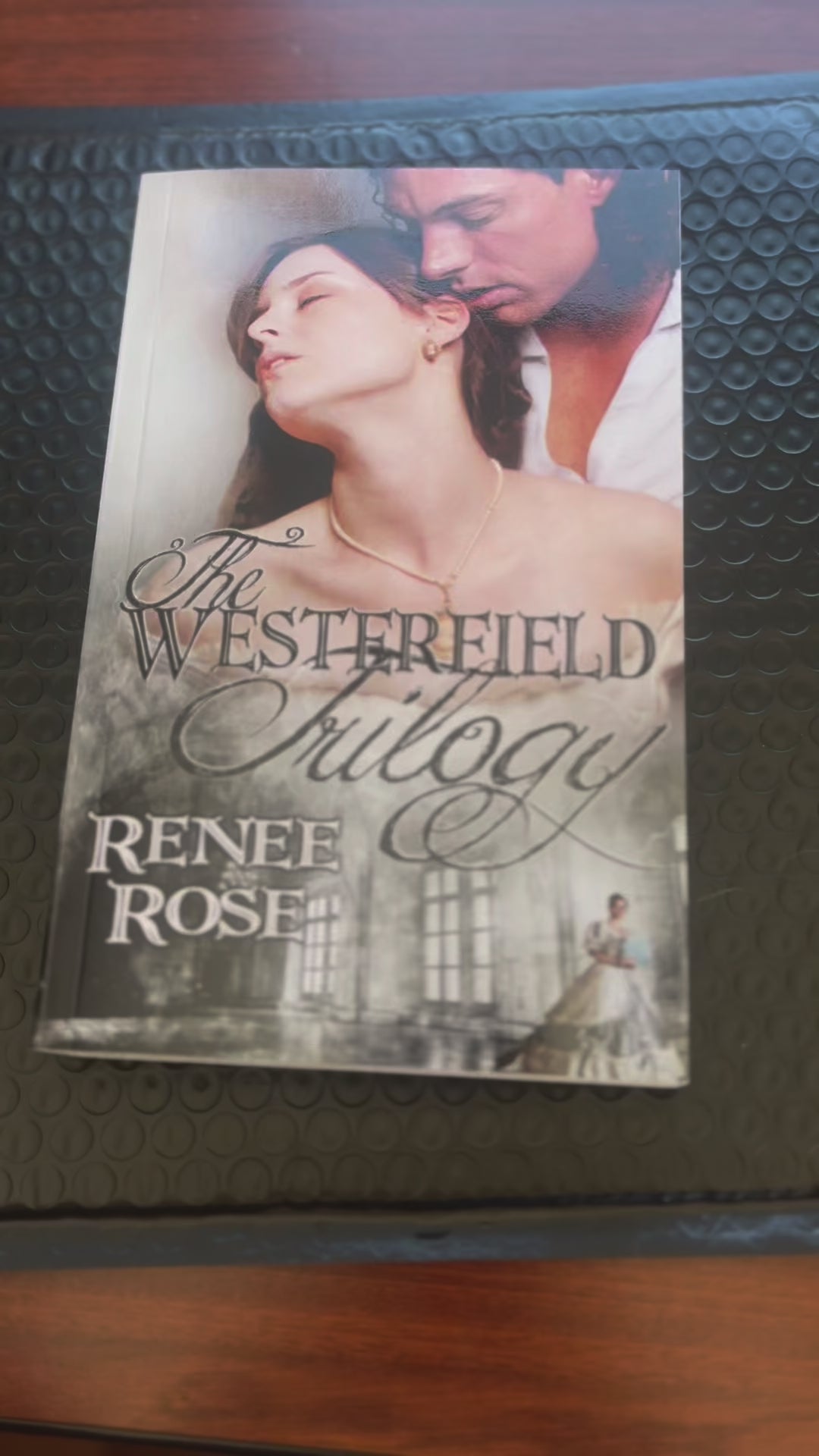 Sped up video. It shows "The Westerfield Trilogy" paperback. A white woman -- Renee Rose -- adds an "Autographed Copy" sticker to the cover, opens the book and signs "Love and scandals, Renee Rose"