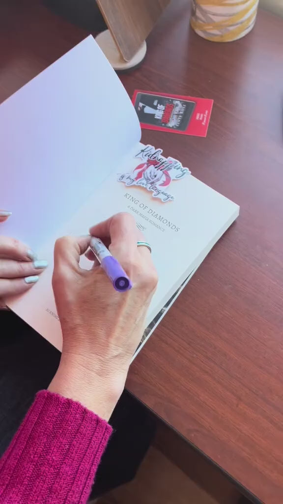 Video of a white woman -- Renee Rose-- showing off the "King of Diamond" and "Mafia Daddy" paperbacks. She writes a note and signs the books before putting them in a pink package and putting on a shipping label. 