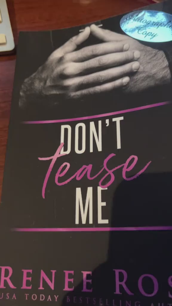 Video of a white woman -- Renee Rose -- opening the "Don't Tease Me" paperback. With a purple thin sharpie she draws a heart, writes "Love and sugar daddy," and signs her name.