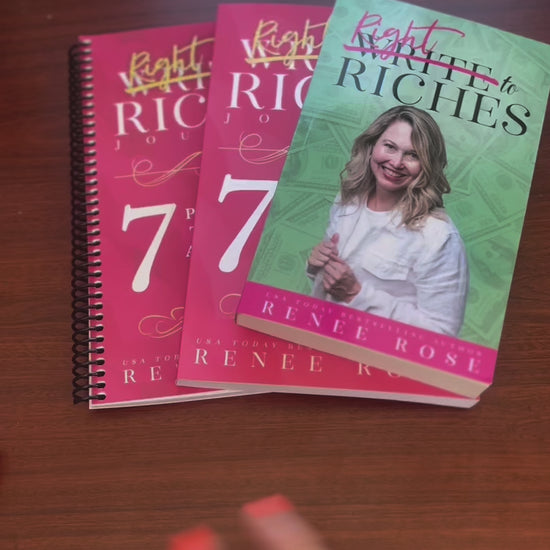 Sped up video. The Write to Riches book, and two versions of the journal are fanned out. A white woman -- Renee Rose -- opens the book, and signs it "ask, believe receive! Renee Rose"