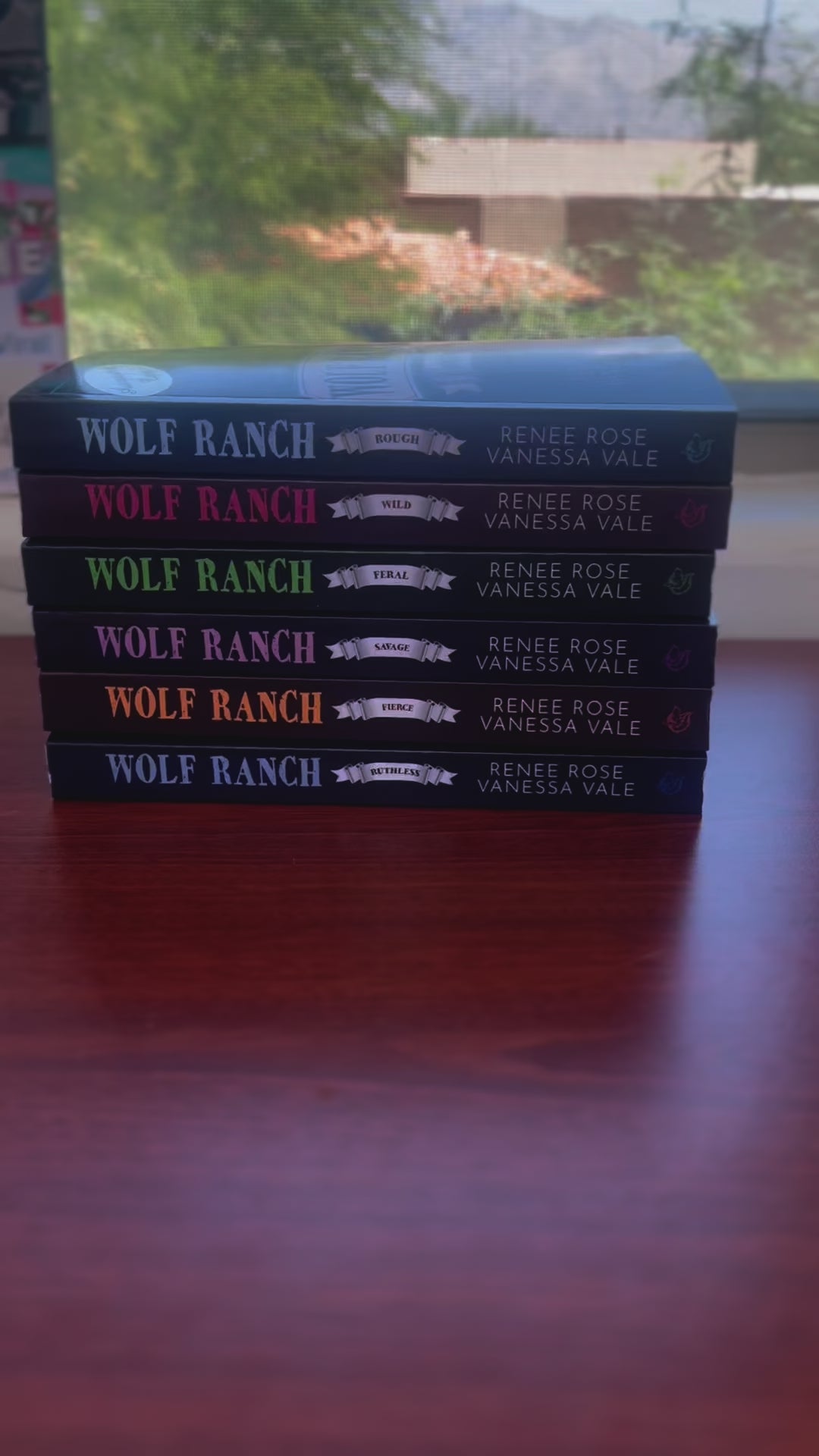 Sped up video. It starts by showing all the books from the Wolf Ranch Series in a stack. A white woman -- Renee Rose-- grabs the top book which has an "Autographed Copy" sticker on it and opens it to show that is has been signed by Renee Rose and Vanessa Vale. 