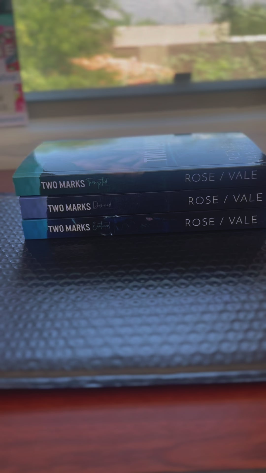 Sped up video. It starts by showing all the books from the Two Marks series in a stack. A white woman -- Renee Rose -- took the top book and signs "Double-wolf love, Renee Rose" ands a sticker of Vanessa Vale's autograph. 