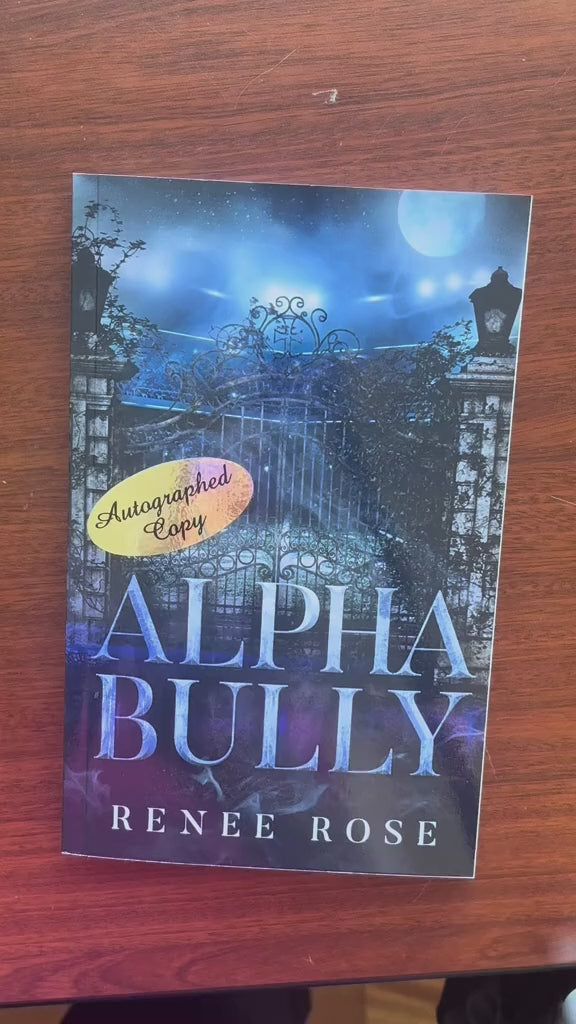 Video of a white woman -- Renee Rose -- opening the "Alpha Bully" book and writing "Love and the (wolf)boy" then signing the paperback. She then puts in some stickers into the book. 