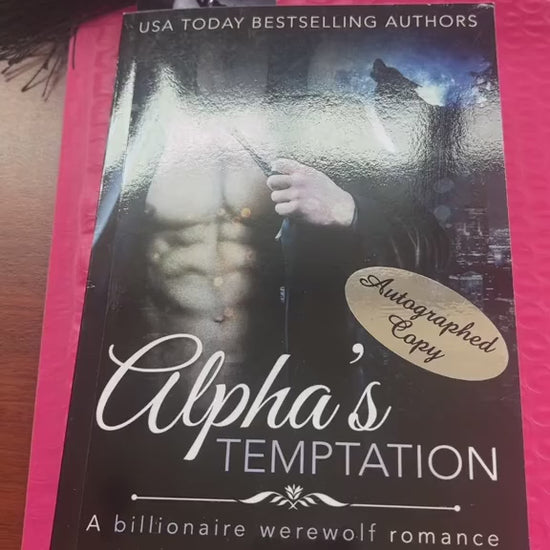 Video of a white woman -- Renee Rose -- showing off a paperback of "Alpha's Temptation." She pulls out stickers and bookmarks out of the book and shows that hand written in a thin purple sharpie is "Love in the elevator," then signed by Renee Rose and Lee Savino. 