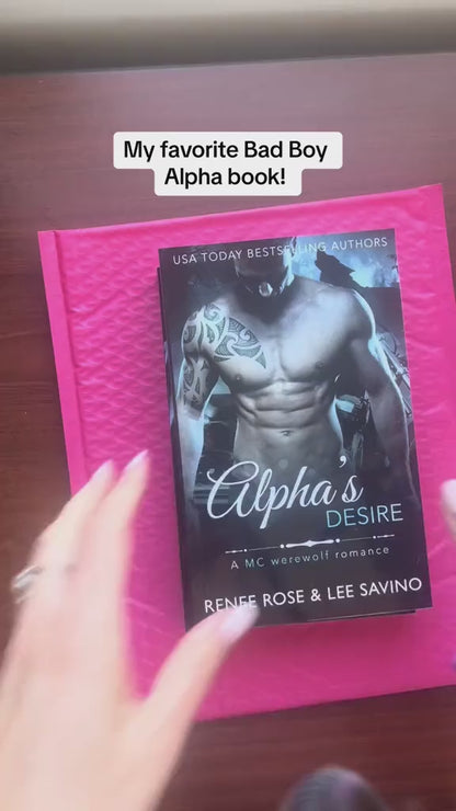 Video of a white woman -- Renee Rose -- showing the "Alphas Desire" book and, with a purple thin sharpie, writes a note and signs the book. She then puts a bookmark and sticker into the book. In black text on the video is "My favorite Bad Boy Alpha book!"