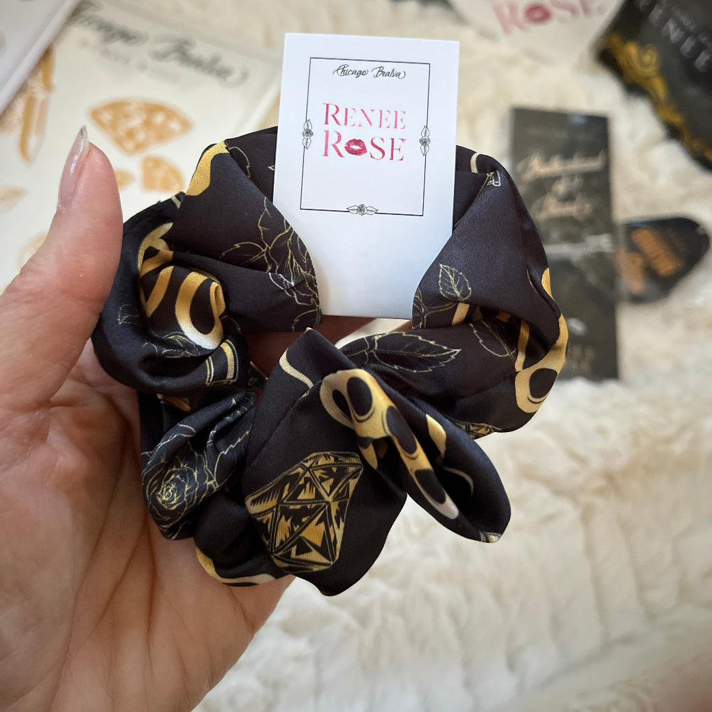 Black scrunchies with gold patterns held by a hand, with 'Renee Rose' branding visible.